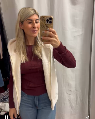 Person taking a mirror selfie wearing a burgundy top, light-colored cardigan, and blue jeans.